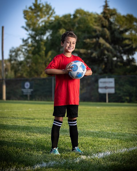 boy soccer player in red jersey poses will ball on soccer field for team photo day