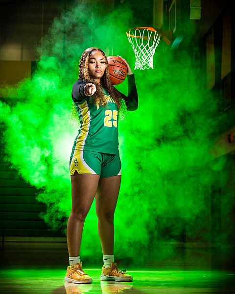 teenage girl basketball player poses with ball and points at the camera for photo day green background and jersey