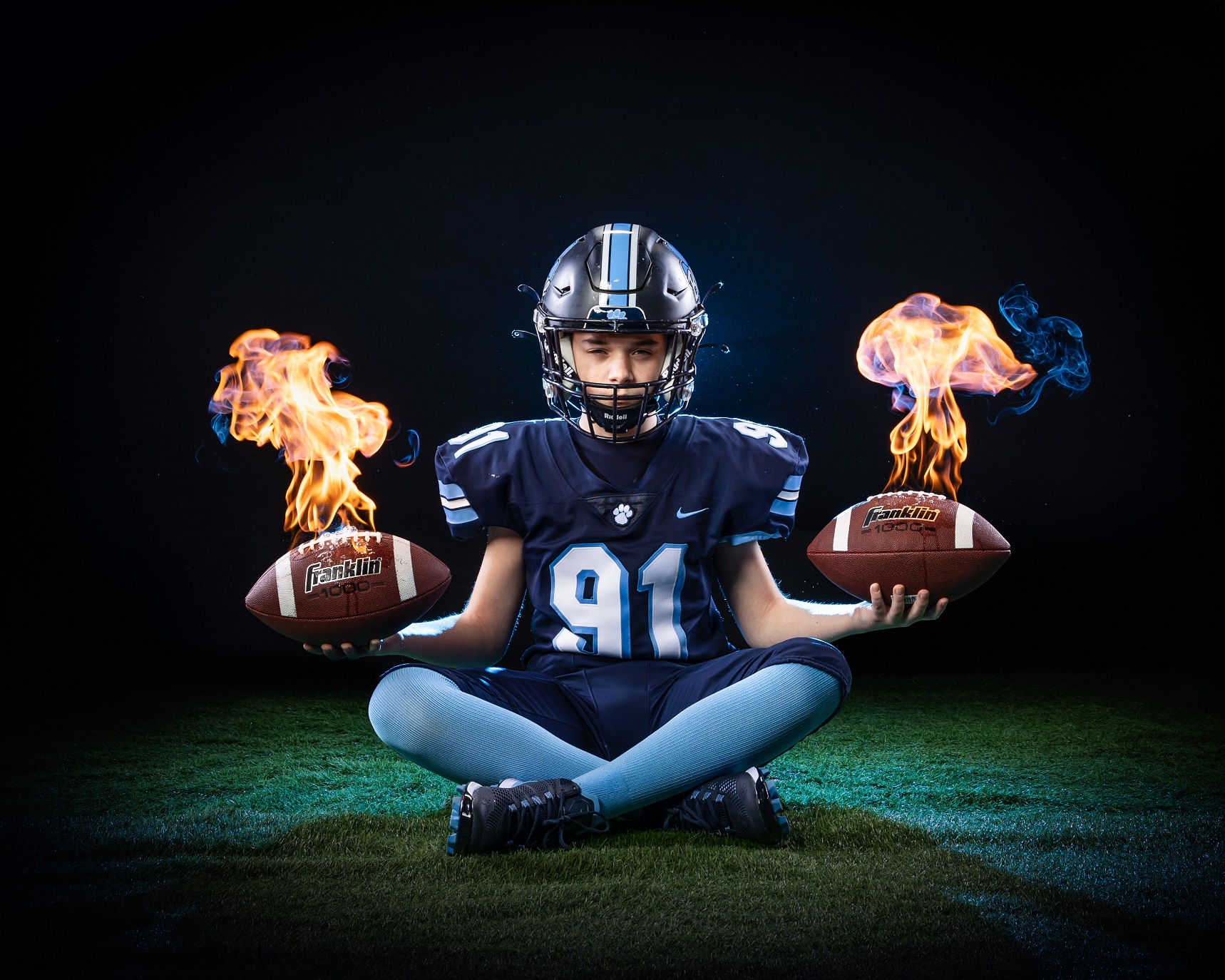 boy football player holds two footballs on fire for media day photoshoot